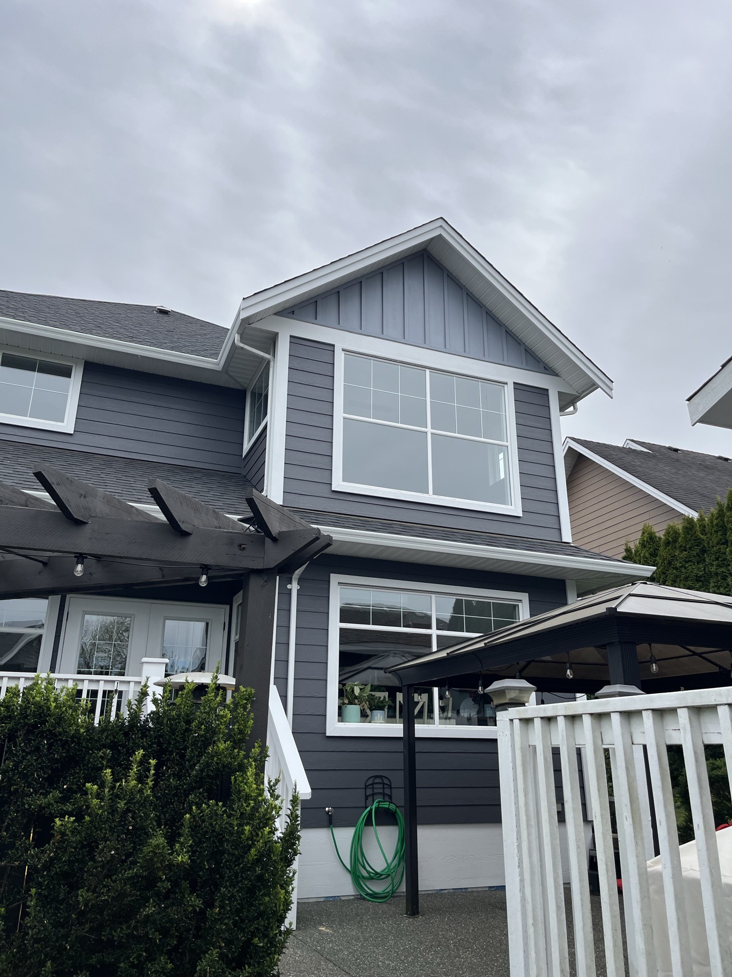 Exterior painting — close view of white-trim windows, dark grey board-and-batten siding and pergola