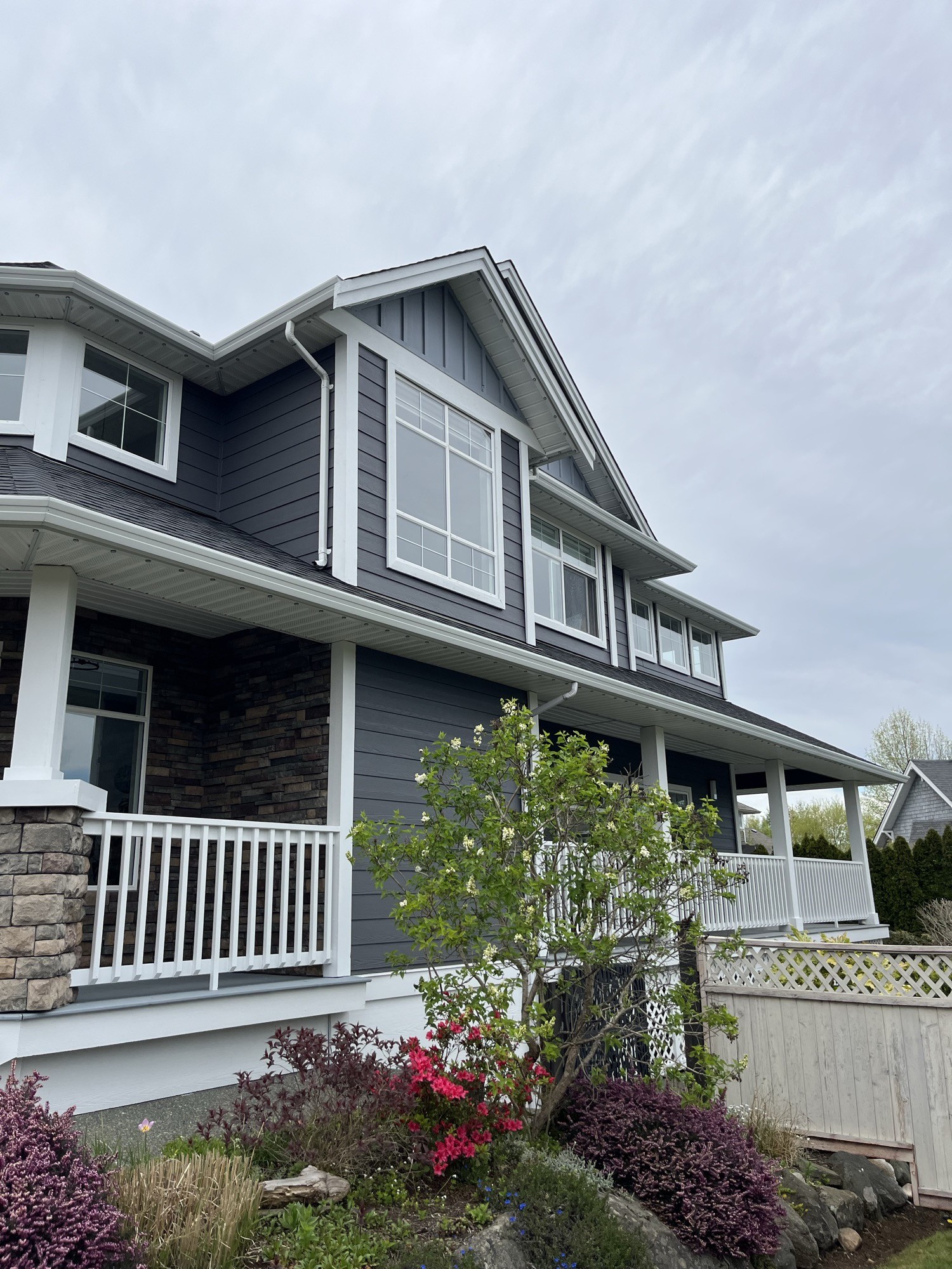 Exterior painting — side angle of dark grey home with white trim, stone porch and garden landscaping
